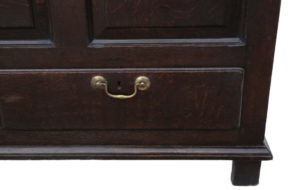 A dark oak Georgian mule chest featuring a carved wave frieze, three fielded front panels, two base drawers with brass handles, and square feet. View XI