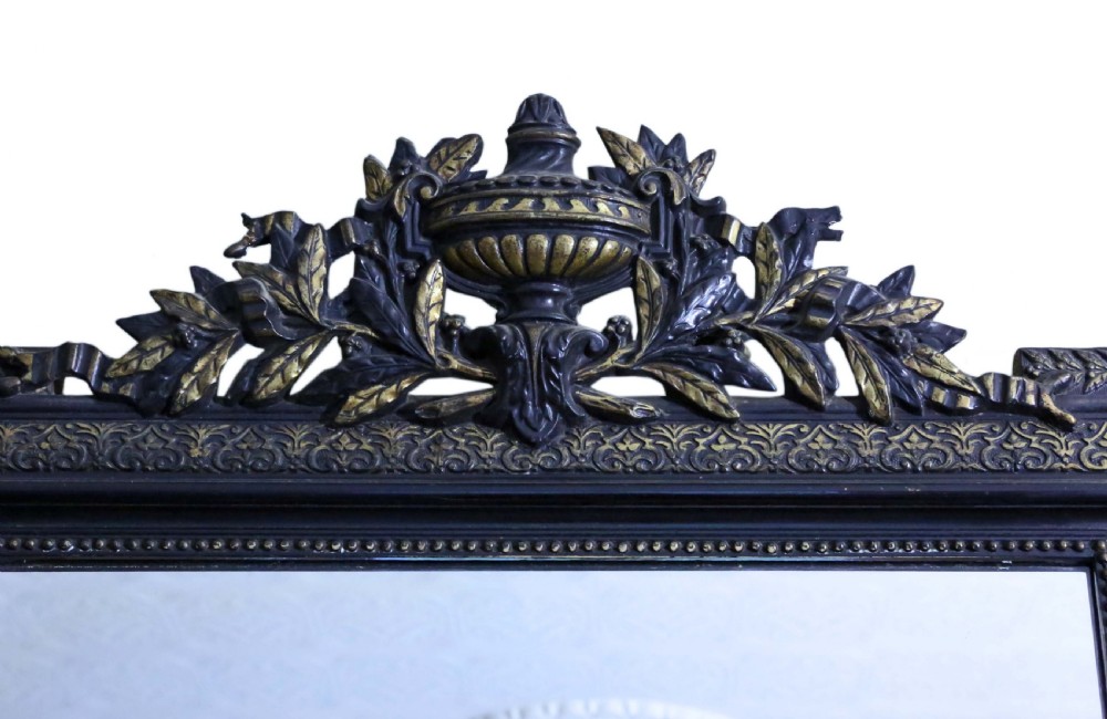 A large rectangular 19th-century ebonised wood overmantel mirror featuring incised gilded borders and a central carved urn pediment flanked by foliate scrollwork. View II