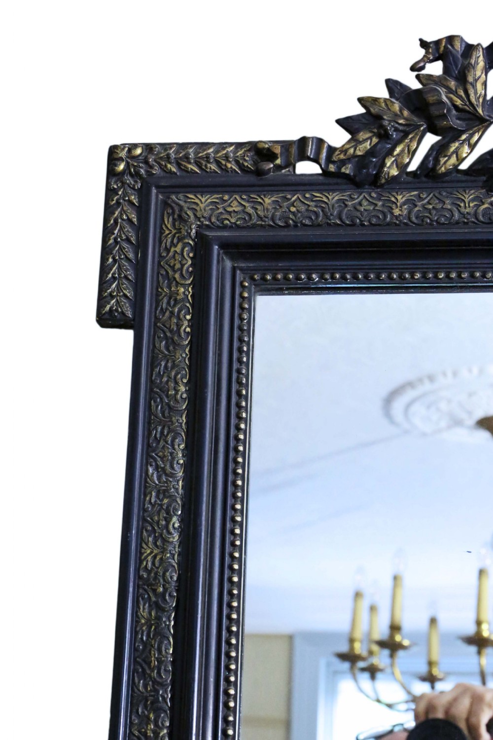 A large rectangular 19th-century ebonised wood overmantel mirror featuring incised gilded borders and a central carved urn pediment flanked by foliate scrollwork. View V