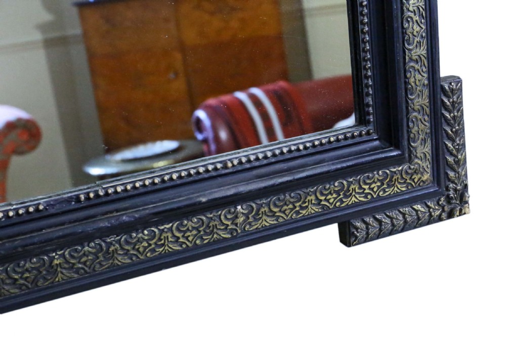 A large rectangular 19th-century ebonised wood overmantel mirror featuring incised gilded borders and a central carved urn pediment flanked by foliate scrollwork. View VII
