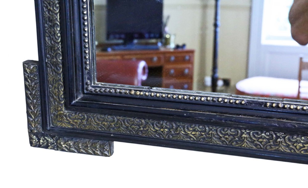 A large rectangular 19th-century ebonised wood overmantel mirror featuring incised gilded borders and a central carved urn pediment flanked by foliate scrollwork. View VIII