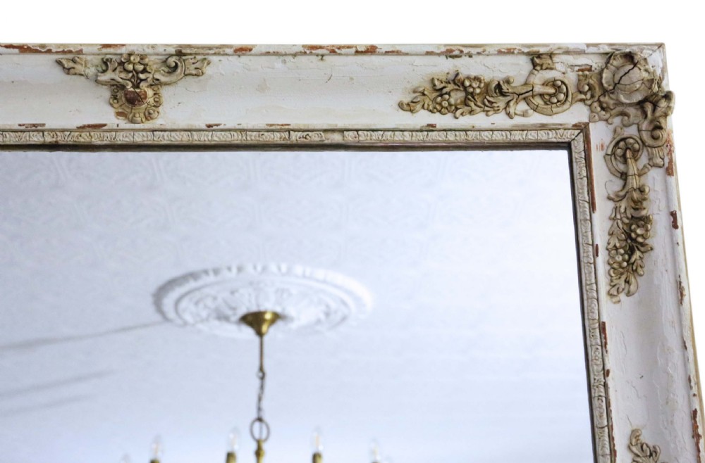 A large nineteenth-century rectangular French overmantle mirror with a cream-painted frame featuring moulded floral scrollwork details and a distressed finish. View IV
