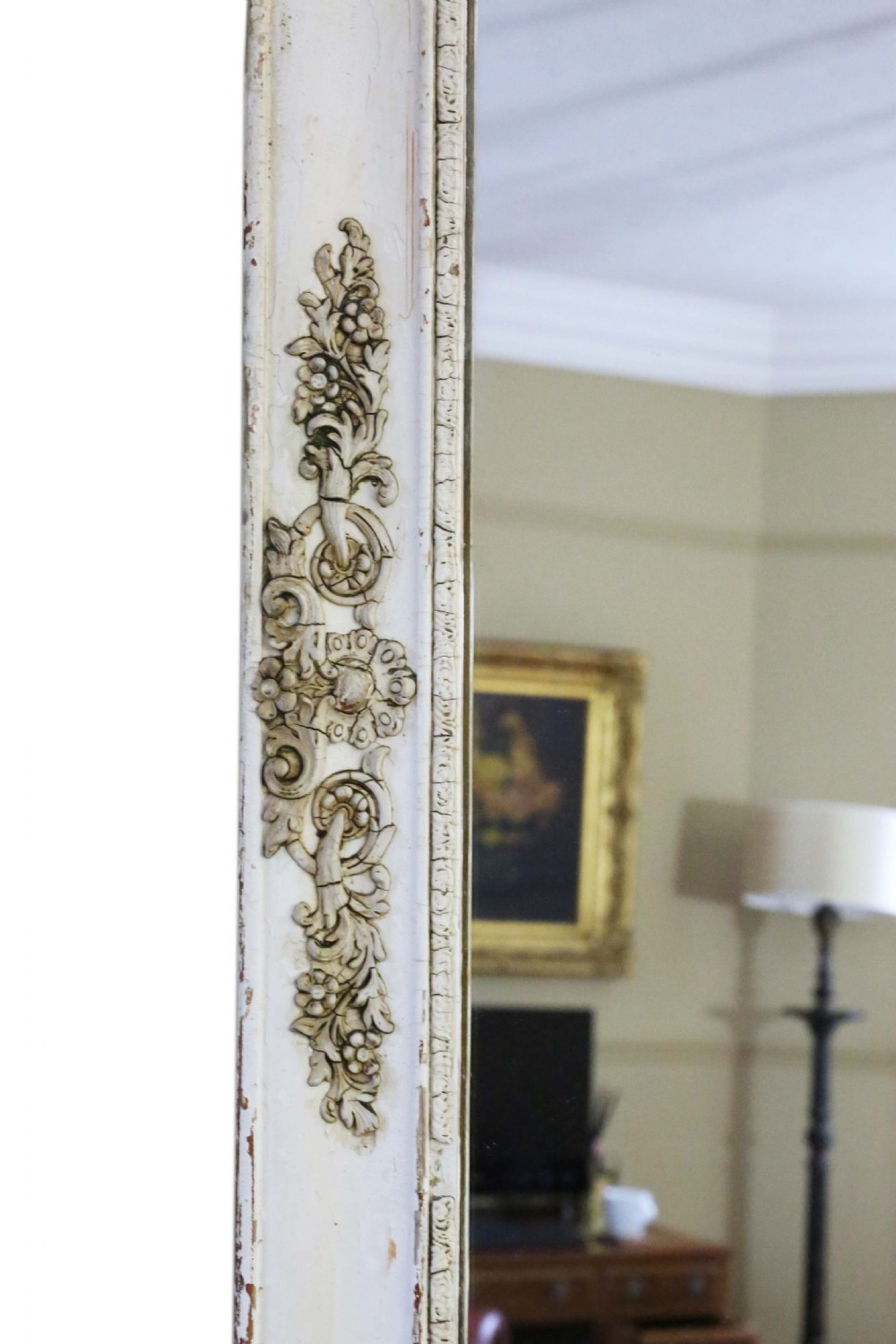 A large nineteenth-century rectangular French overmantle mirror with a cream-painted frame featuring moulded floral scrollwork details and a distressed finish. View VII
