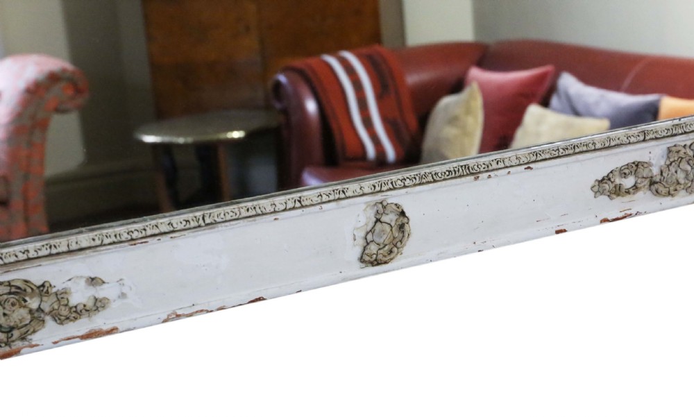 A large nineteenth-century rectangular French overmantle mirror with a cream-painted frame featuring moulded floral scrollwork details and a distressed finish. View VIII