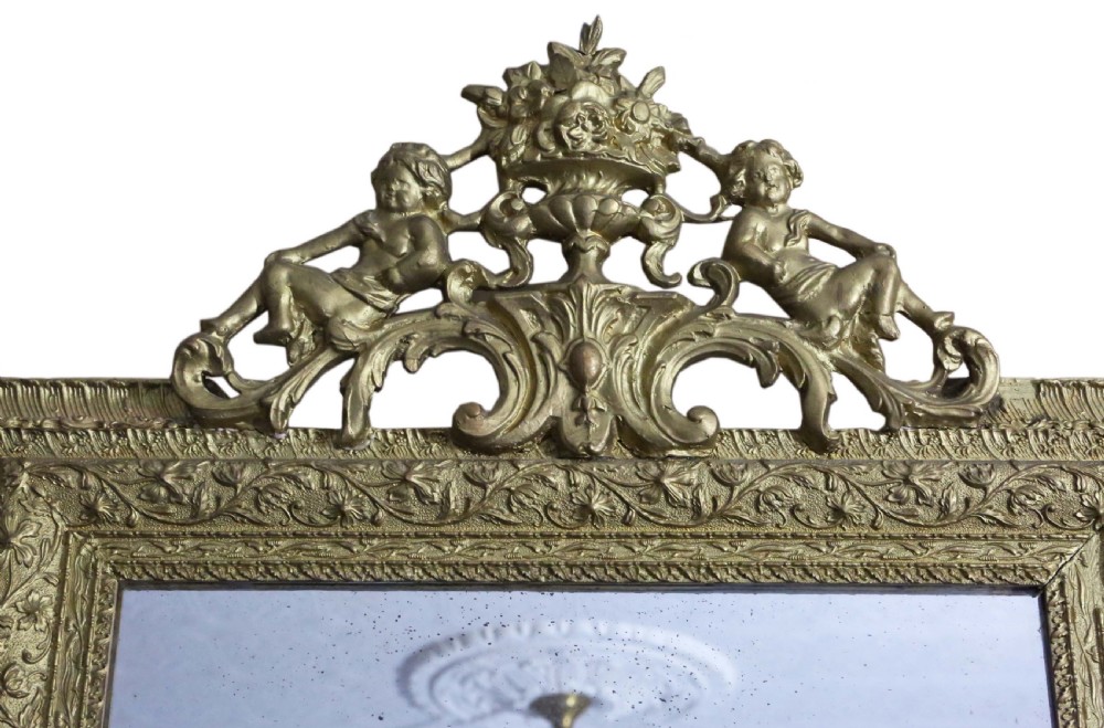 A large 19th-century rectangular giltwood wall mirror with an ornate crest depicting cherubs and an urn above floral moulding. View II