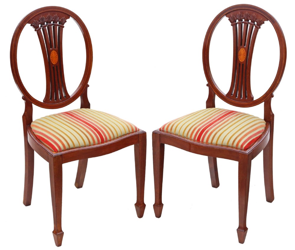 A pair of Edwardian Georgian Revival mahogany side chairs with circular backrests, carved central splats, satinwood marquetry inlays, and striped fabric seats.