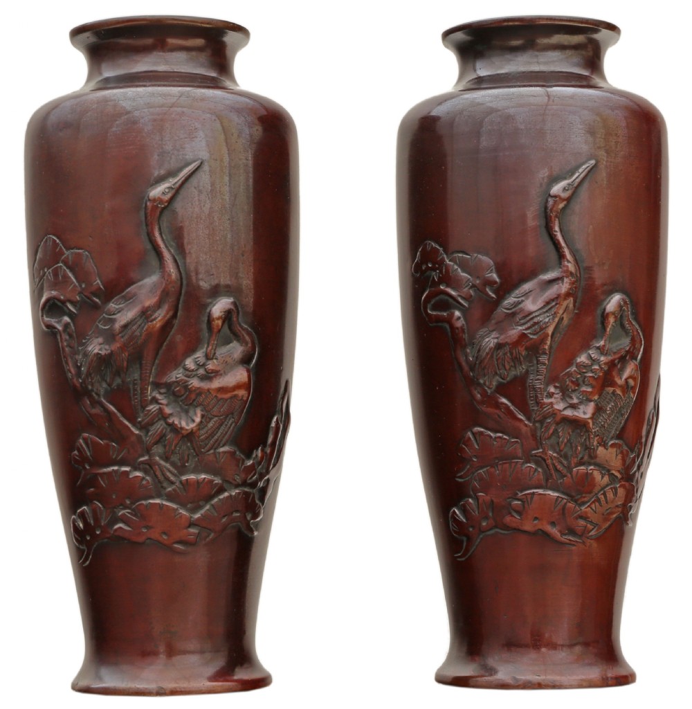 Pair of Japanese bronze vases featuring raised relief carving of cranes standing amongst foliage against a rich brown patina.