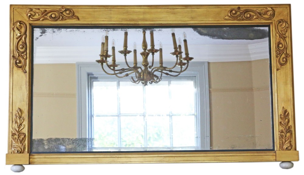 A large rectangular 19th-century giltwood overmantel wall mirror featuring carved foliage corners and a foxed glass plate resting on ceramic feet.