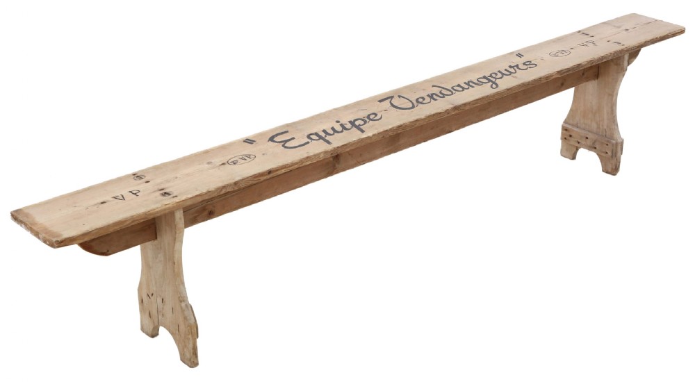 A long, pale timber garden bench featuring stencilled black text along the top plank and shaped trestle legs.