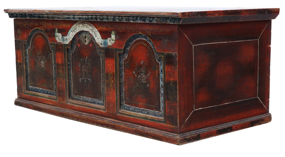 An antique rectangular wooden coffer with a natural pine lid and a red and dark green painted front featuring three arched panels with floral motifs. View V