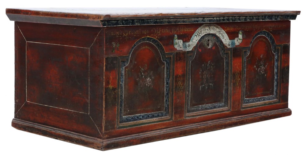 An antique rectangular wooden coffer with a natural pine lid and a red and dark green painted front featuring three arched panels with floral motifs. View VI