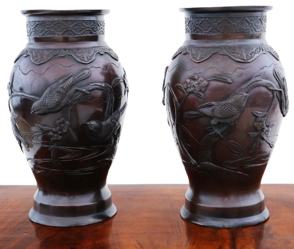 A pair of dark brown patinated Japanese Meiji period bronze vases featuring high relief carvings of birds perched on branches with geometric borders.