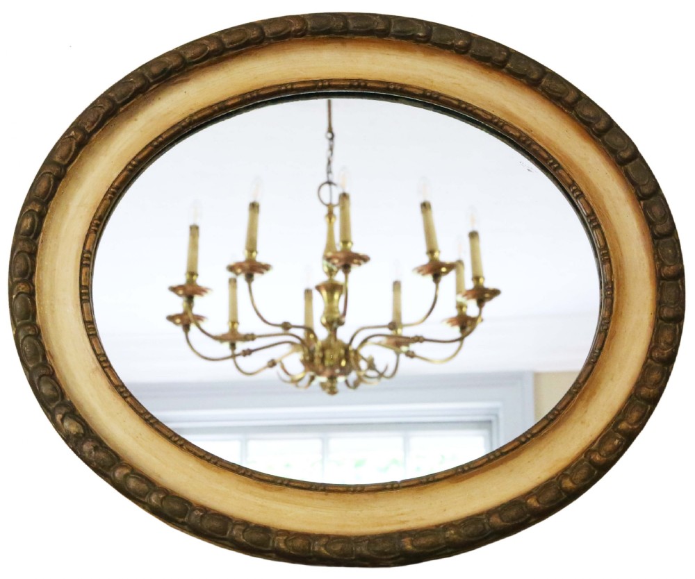 An oval 19th-century wall mirror featuring a carved outer gilt border surrounding a broad cream-painted inner frame. View IV