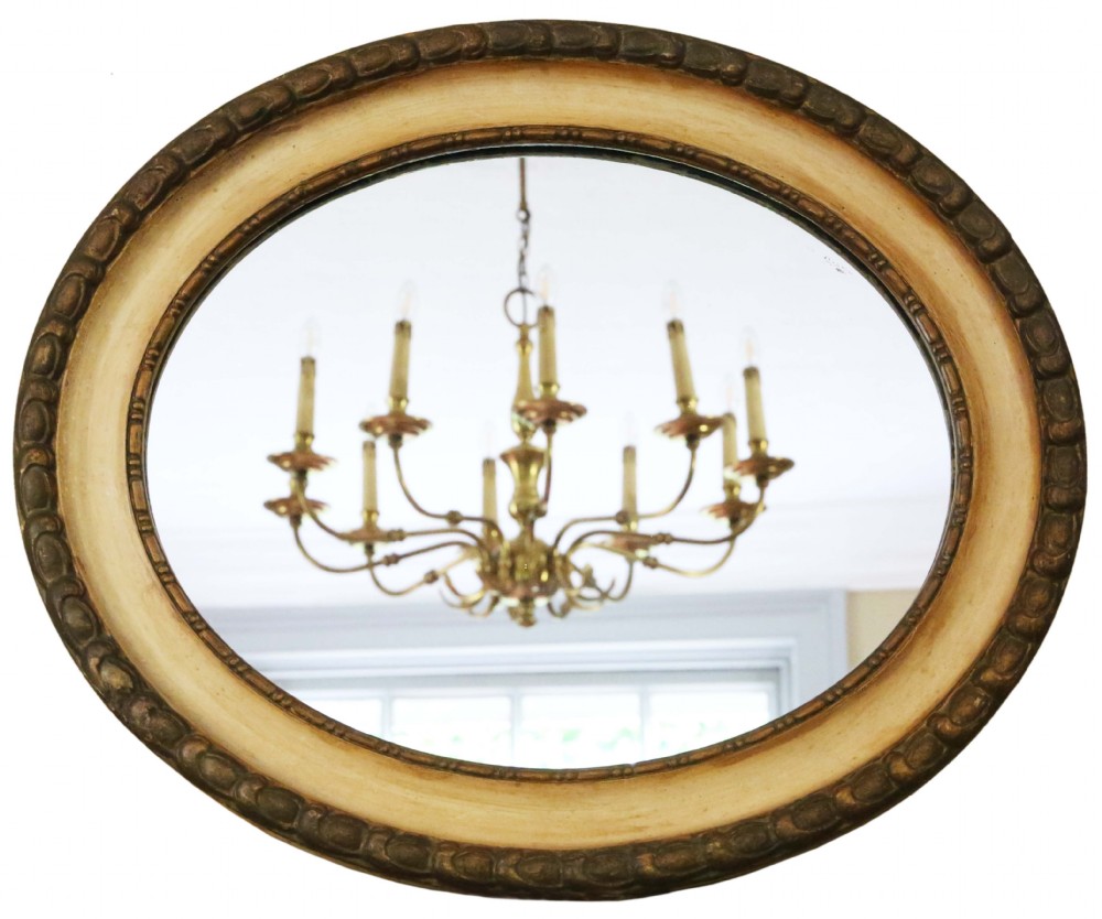 An oval 19th-century wall mirror featuring a carved outer gilt border surrounding a broad cream-painted inner frame.