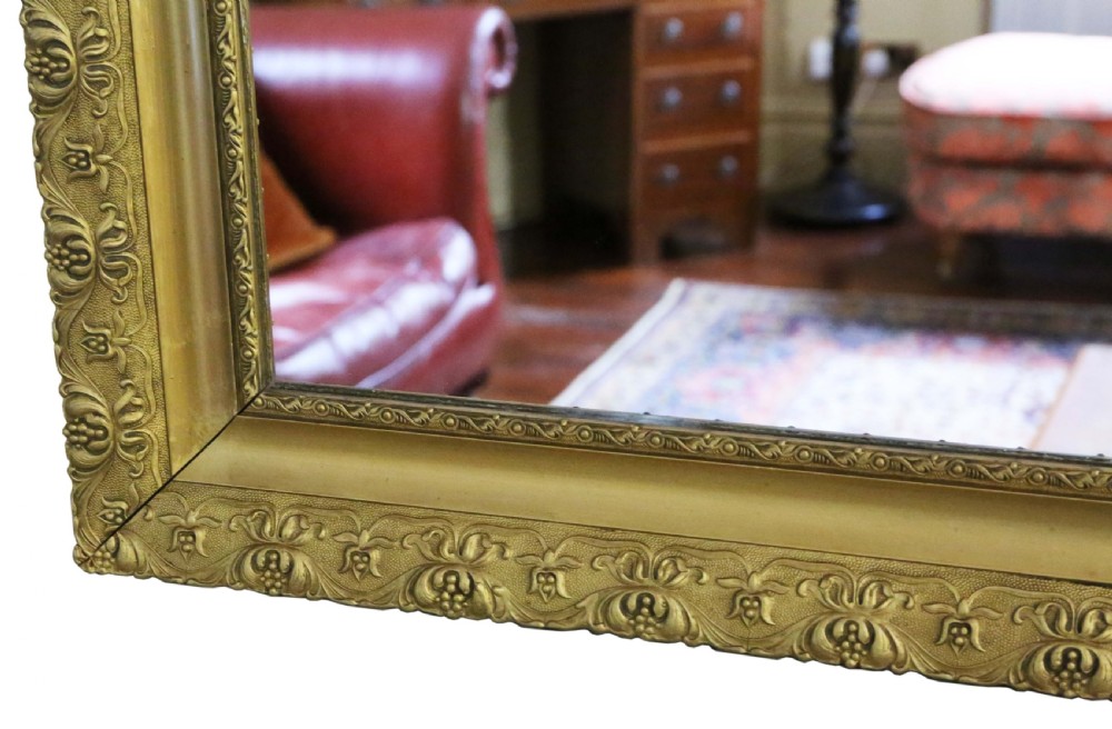 A large rectangular antique gilt overmantel mirror featuring detailed moulded borders and a gold finish. View V