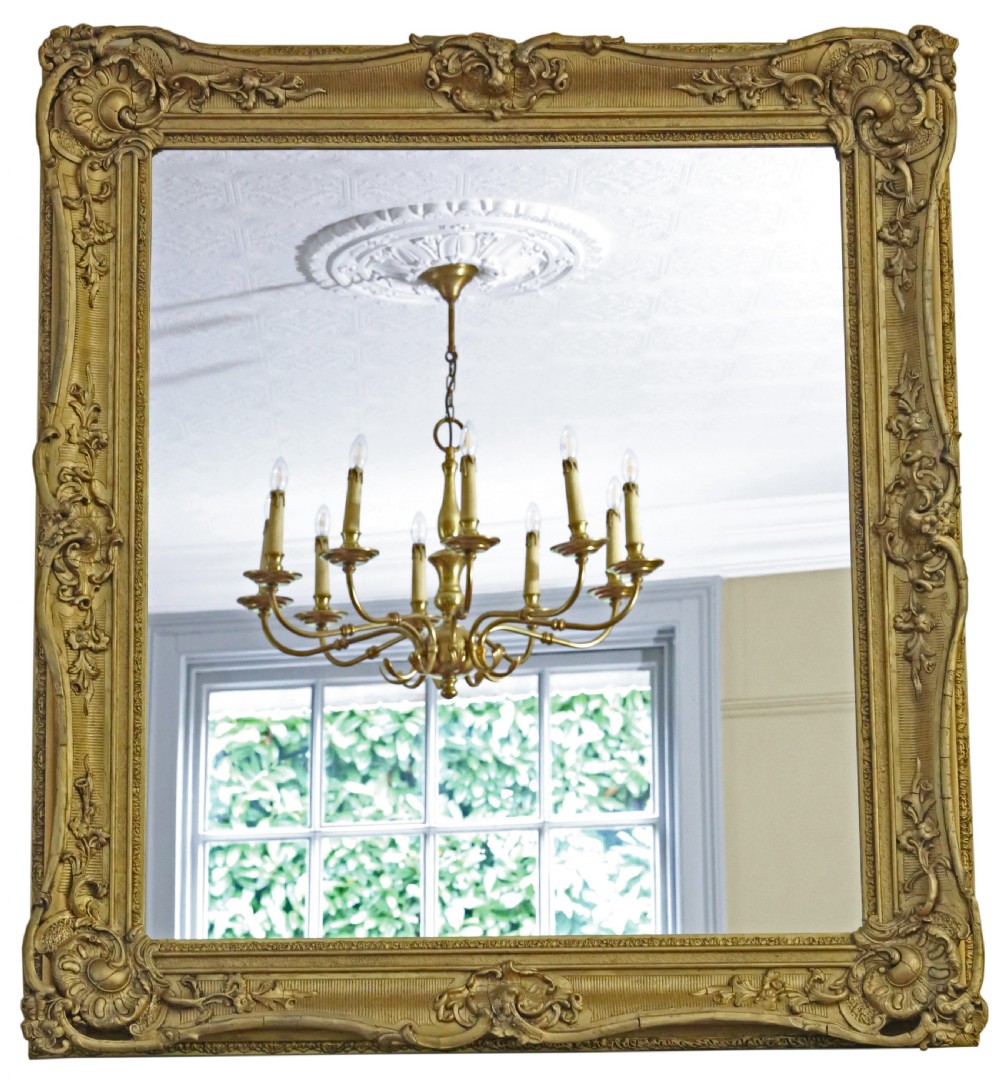 A large 19th-century rectangular giltwood overmantel mirror featuring ornate scrollwork, corner shell motifs, and a moulded inner border.