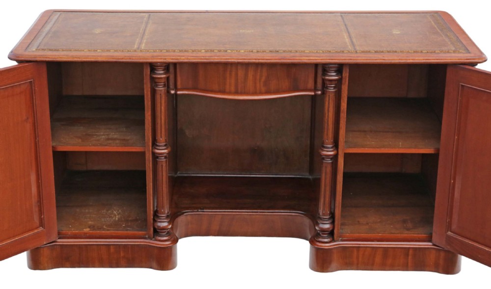 A 19th-century mahogany twin pedestal writing desk featuring a gold-tooled leather inset top, twin cupboard doors flanked by turned columns, and a central kneehole. View V