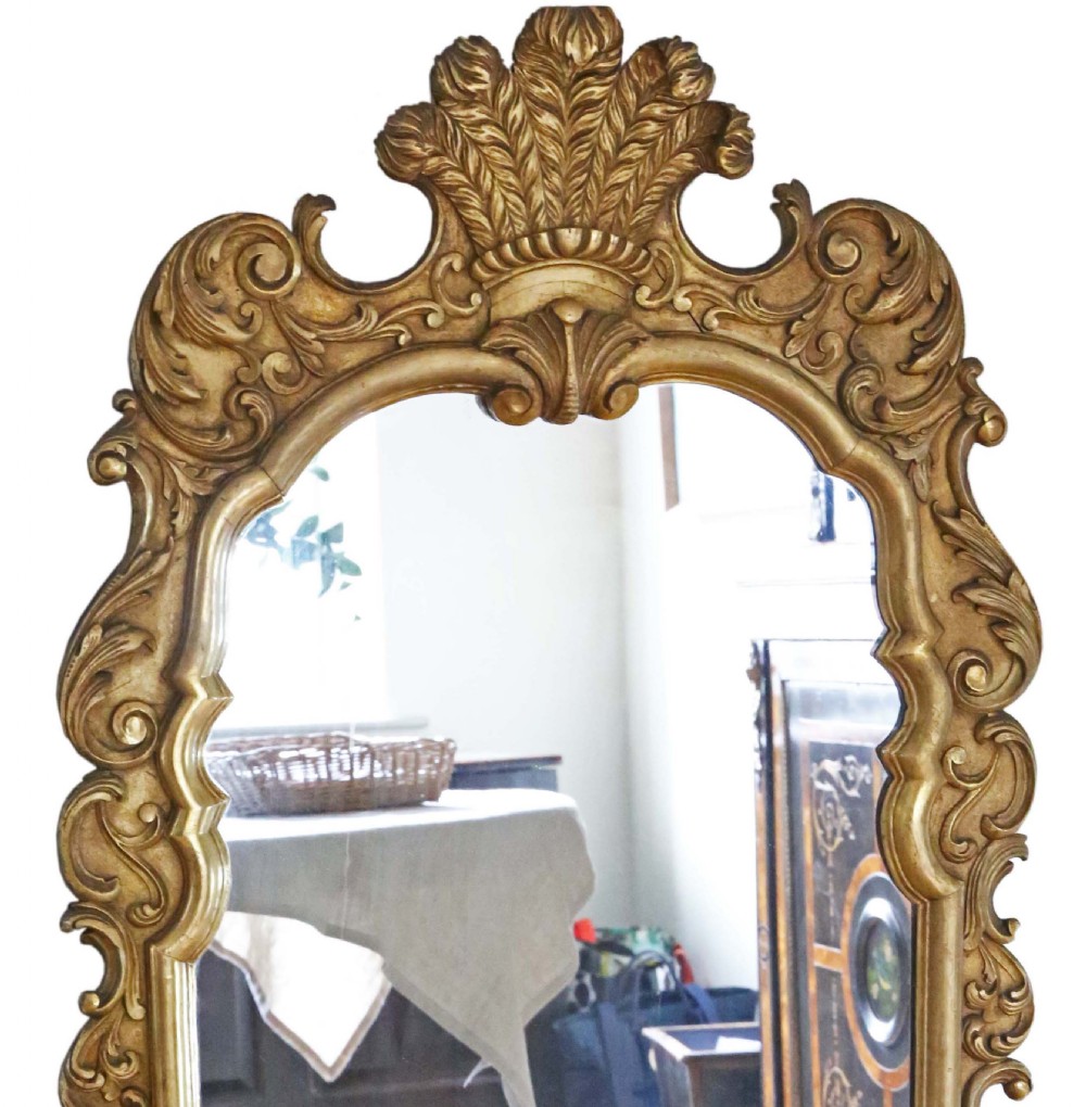 A tall Rococo Revival giltwood overmantel wall mirror featuring an arched top crested with carved plume motifs and surrounded by scrolling foliage. View II