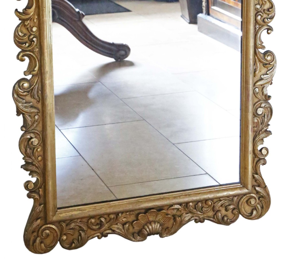 A tall Rococo Revival giltwood overmantel wall mirror featuring an arched top crested with carved plume motifs and surrounded by scrolling foliage. View IV