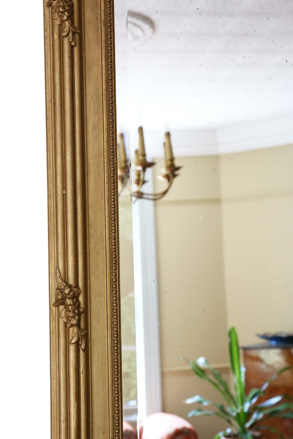 Large antique giltwood overmantel wall mirror featuring an ornate ribbon crest motif, floral swags, molded frame, and bevelled glass plate. View V
