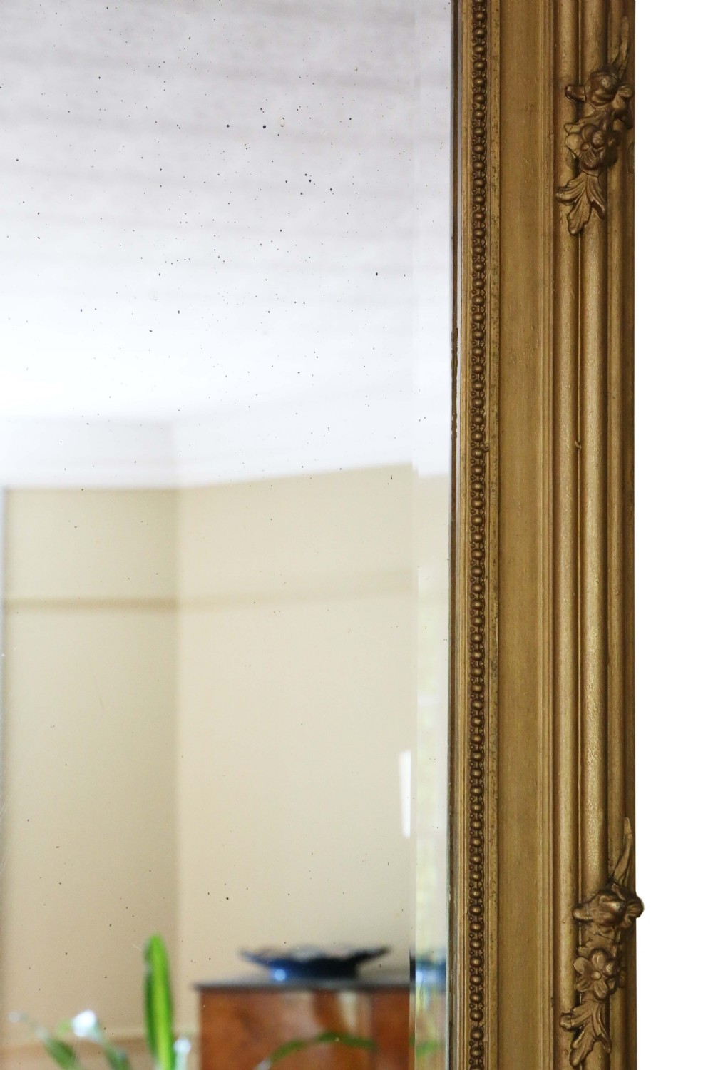 Large antique giltwood overmantel wall mirror featuring an ornate ribbon crest motif, floral swags, molded frame, and bevelled glass plate. View VI