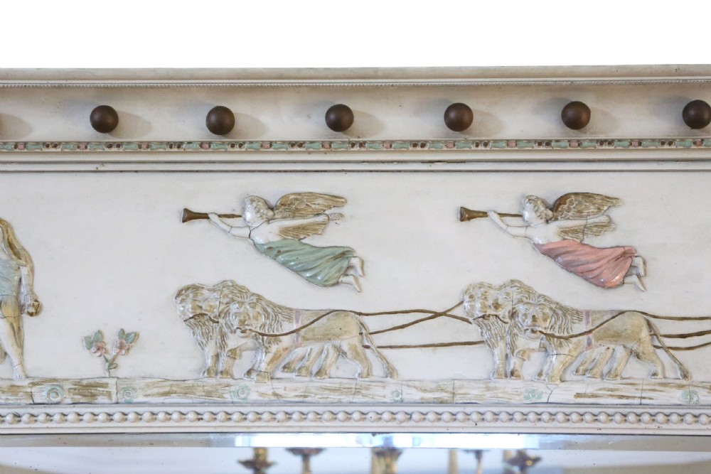 A 19th-century Regency overmantel mirror featuring an off-white painted frame with a classical chariot relief frieze above three mirror plates flanked by fluted pilasters. View IV