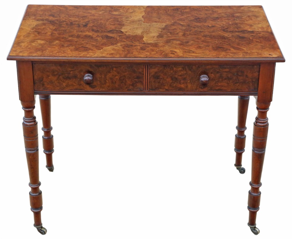 A nineteenth-century burr walnut writing table featuring a figured veneer top, two frieze drawers with turned wooden knobs, and tapering turned legs on brass castors. View VI
