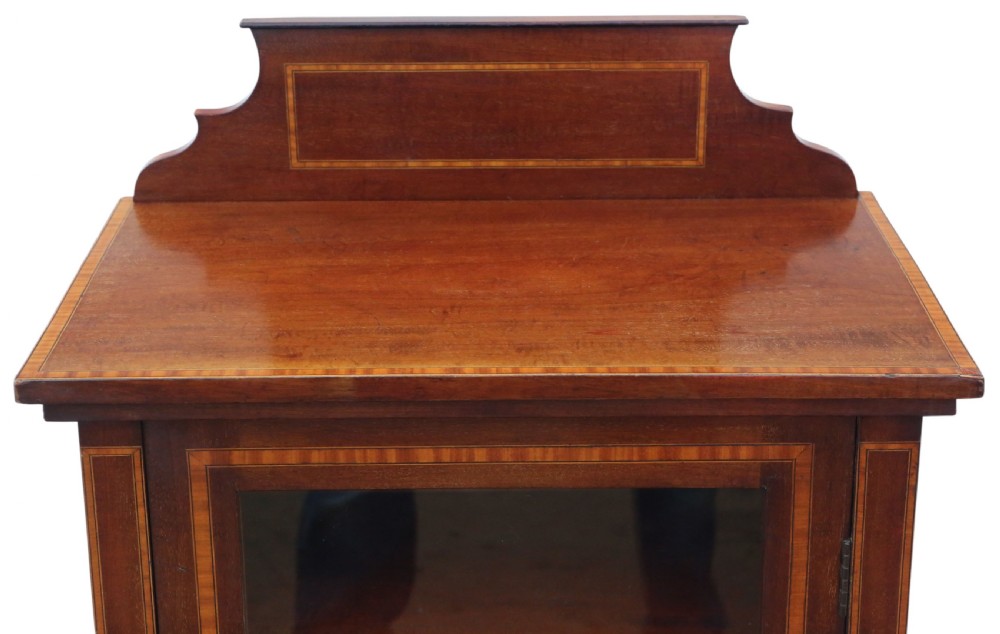 An Edwardian mahogany display cabinet featuring a single glazed door with light wood inlay, resting on tapered legs with brass castors. View VII
