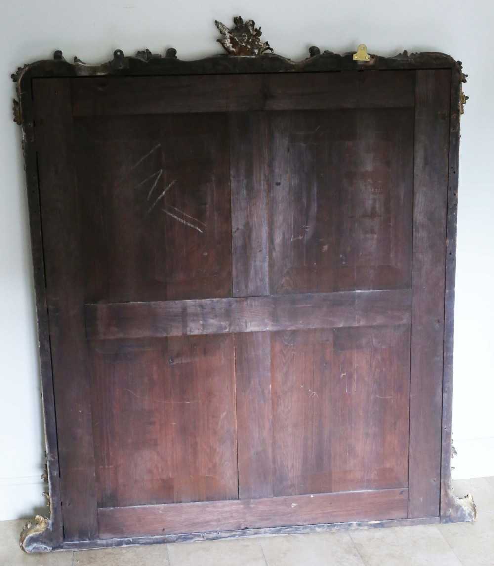 A large nineteenth-century giltwood overmantel mirror featuring an arched frame topped with a carved crest motif and lower foliage flourishes. View IX