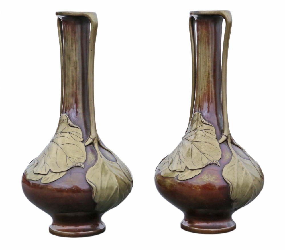 A pair of tall Japanese Meiji era mixed metal bronze vases featuring elongated necks, handles, and cast leaf relief details around the bulbous base.