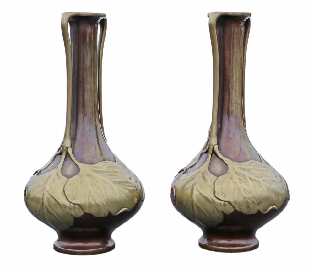 A pair of tall Japanese Meiji era mixed metal bronze vases featuring elongated necks, handles, and cast leaf relief details around the bulbous base. View V