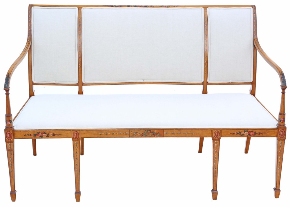 A late 19th-century painted satinwood sofa featuring cream fabric upholstery, three backrest panels, curved armrests, and hand-painted floral detailing on the timber frame.