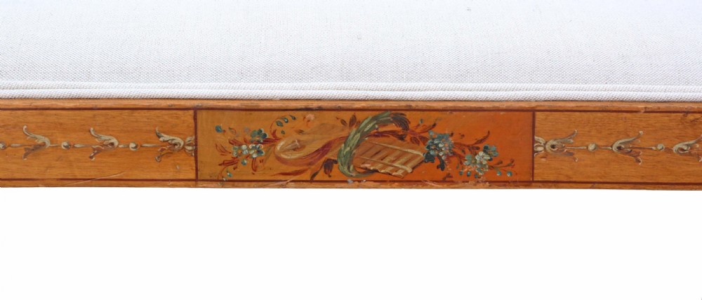 A late 19th-century painted satinwood sofa featuring cream fabric upholstery, three backrest panels, curved armrests, and hand-painted floral detailing on the timber frame. View VI