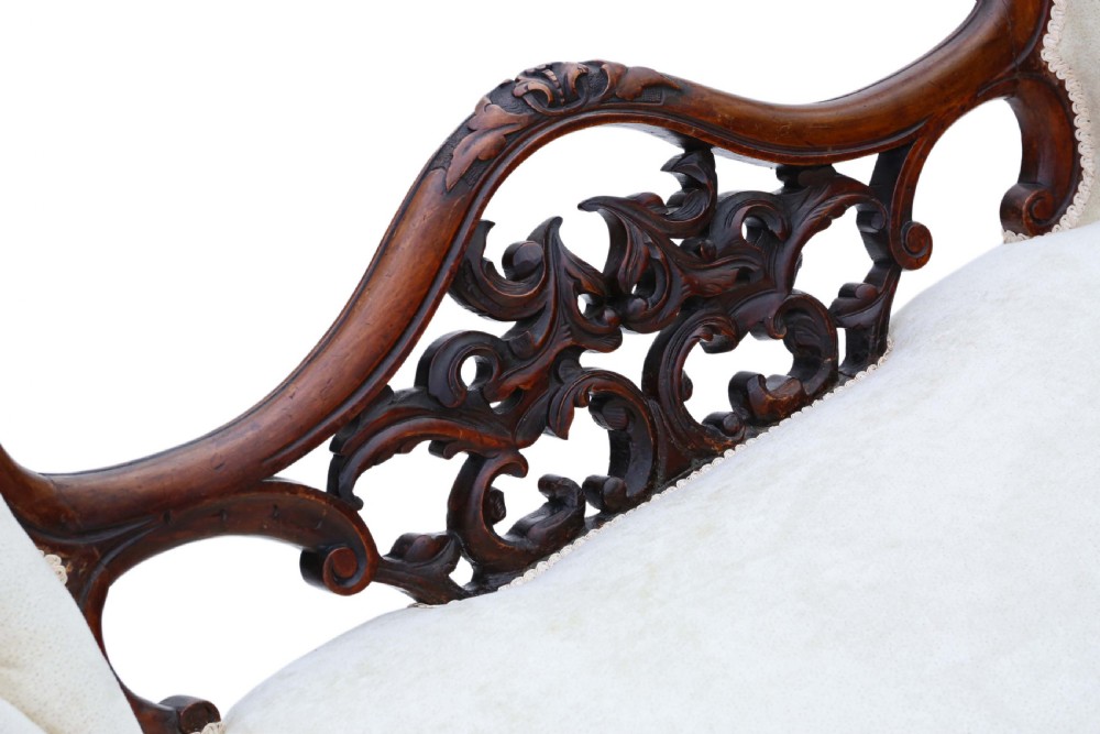 A mid-19th century Victorian carved walnut chaise longue with button-backed cream fabric upholstery, pierced floral backrest carving, and cabriole legs on castors. View IV