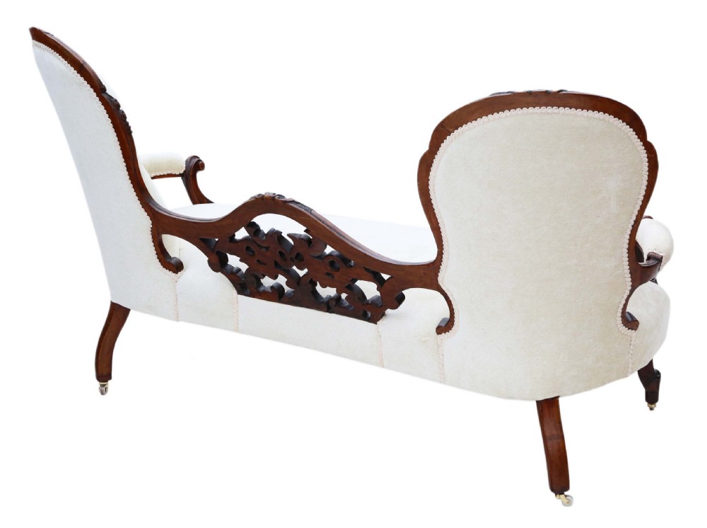 A mid-19th century Victorian carved walnut chaise longue with button-backed cream fabric upholstery, pierced floral backrest carving, and cabriole legs on castors. View X