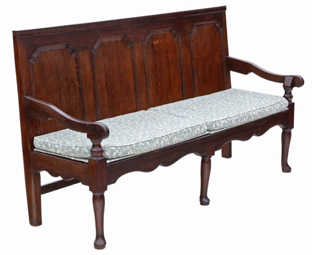 An 18th-century Georgian dark oak settle bench with a high fielded-panel back, shaped apron, turned front legs, and a light-coloured floral cushion.