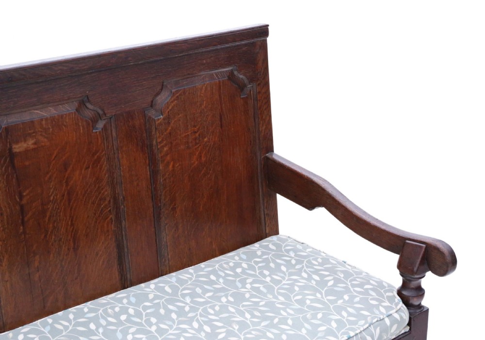 An 18th-century Georgian dark oak settle bench with a high fielded-panel back, shaped apron, turned front legs, and a light-coloured floral cushion. View II