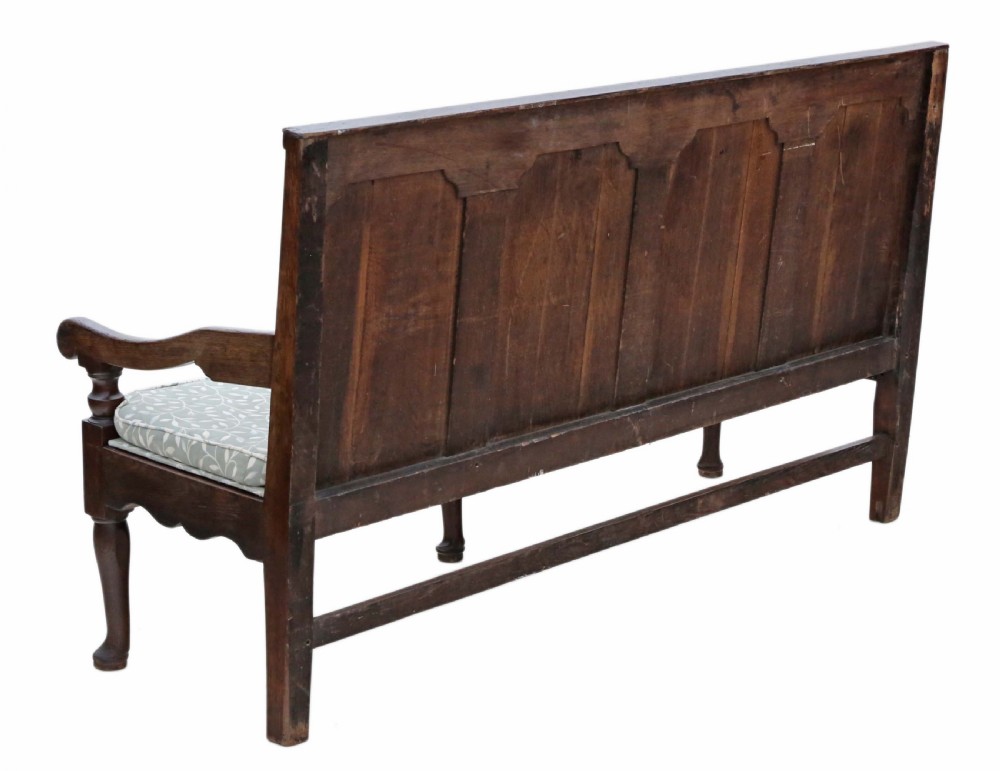 An 18th-century Georgian dark oak settle bench with a high fielded-panel back, shaped apron, turned front legs, and a light-coloured floral cushion. View V