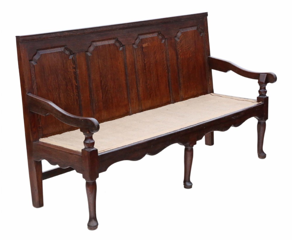 An 18th-century Georgian dark oak settle bench with a high fielded-panel back, shaped apron, turned front legs, and a light-coloured floral cushion. View VI