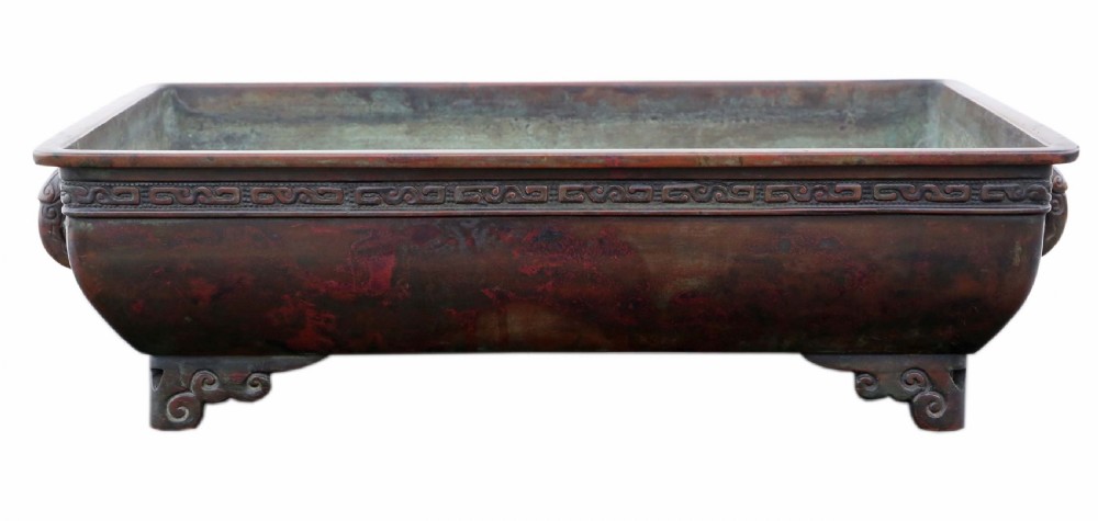 A rectangular dark reddish brown patinated bronze planter with a carved key fret rim border, side handles, and four scroll feet.