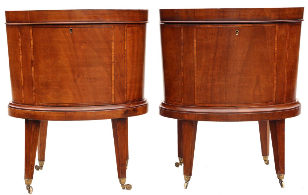 A pair of 19th-century oval mahogany cellarettes with line inlay, escutcheons, tapered legs, and brass castors.