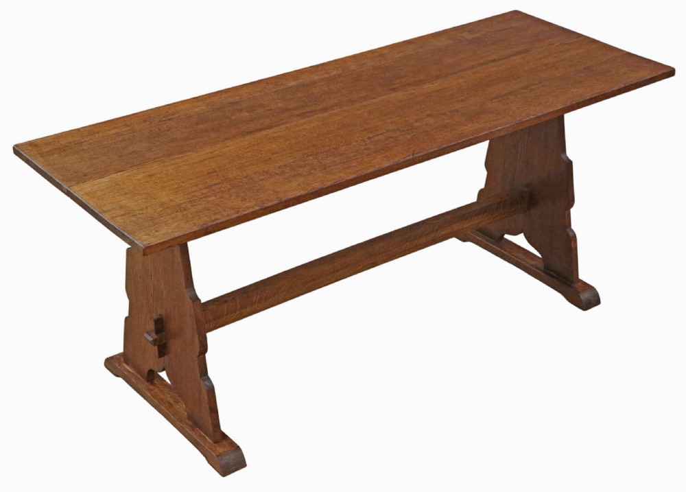An antique late 19th-century solid oak Arts and Crafts refectory dining table featuring shaped trestle ends and a tusked tenon stretcher.