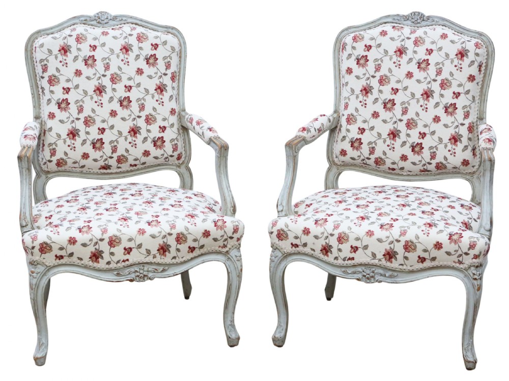 A pair of antique French Louis XV style open armchairs with carved light grey painted frames and floral print upholstery.