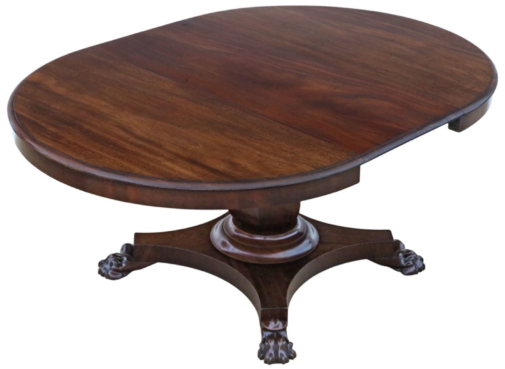 An antique nineteenth-century dark mahogany extending dining table featuring an oval top set on a central pedestal base with four carved paw feet.