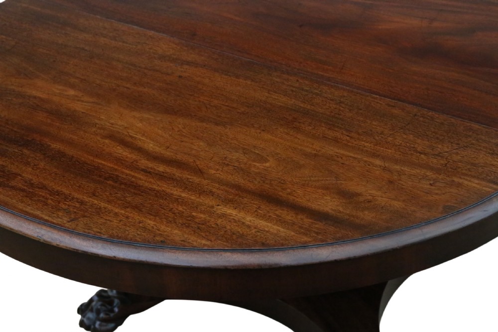 An antique nineteenth-century dark mahogany extending dining table featuring an oval top set on a central pedestal base with four carved paw feet. View V