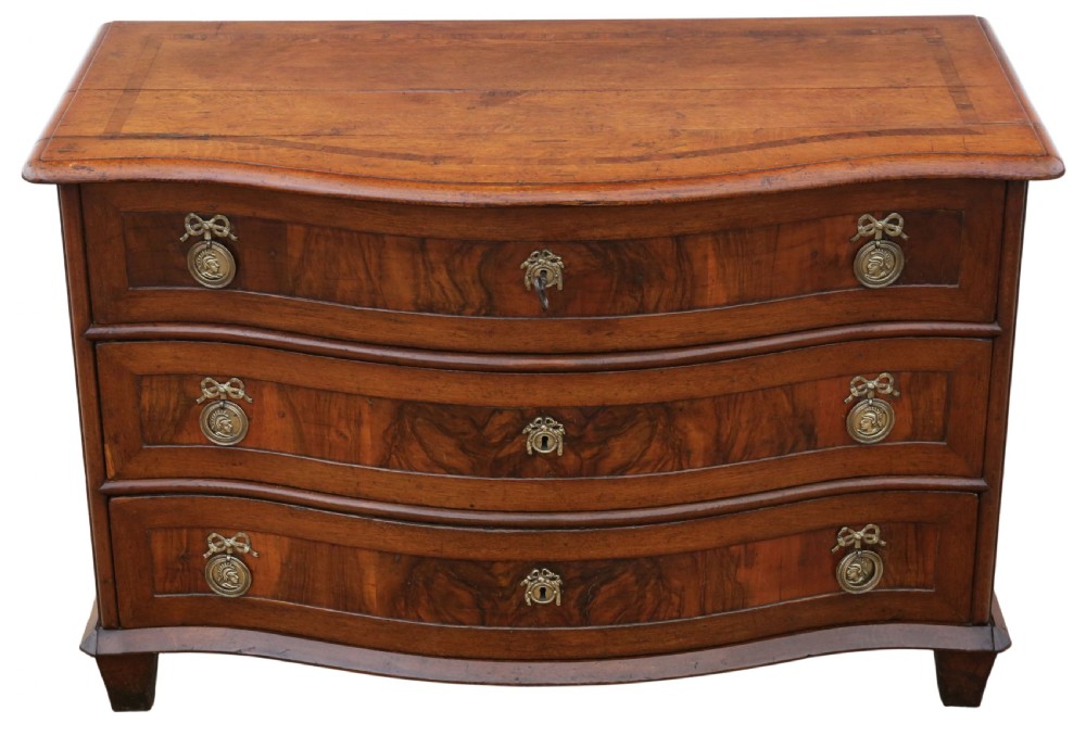 An 18th-century Continental oak and walnut chest of drawers featuring a serpentine front, crossbanded top, and three drawers with ornamental brass handles.