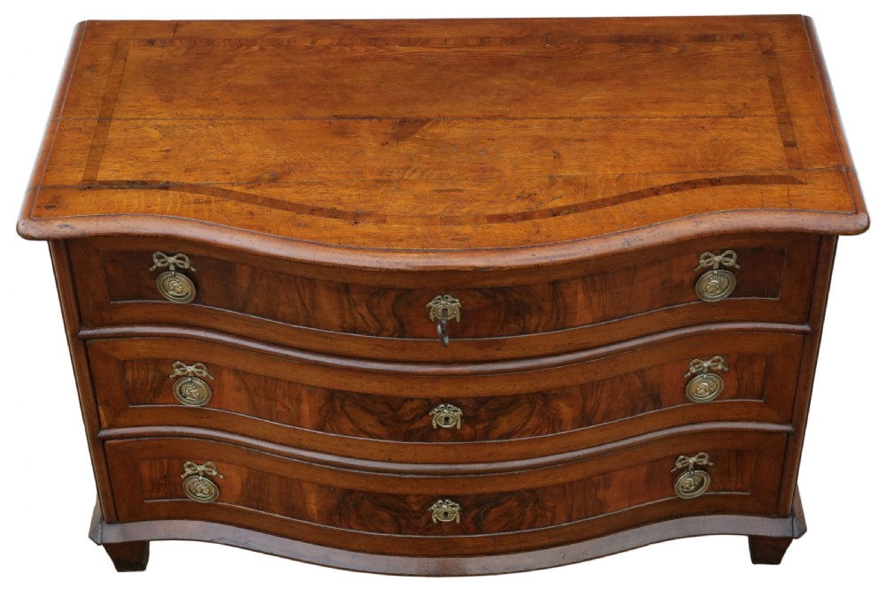 An 18th-century Continental oak and walnut chest of drawers featuring a serpentine front, crossbanded top, and three drawers with ornamental brass handles. View II