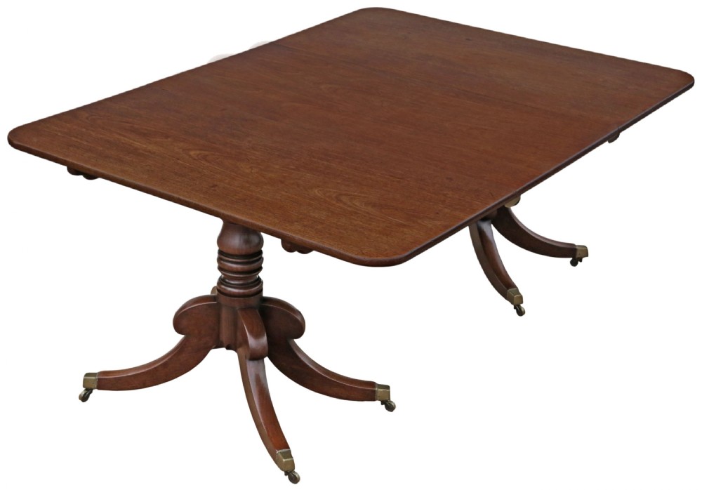 An early 19th-century Georgian mahogany twin pedestal dining table featuring turned columns, splayed legs, and brass cap castors.