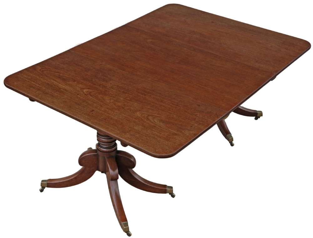 An early 19th-century Georgian mahogany twin pedestal dining table featuring turned columns, splayed legs, and brass cap castors. View II