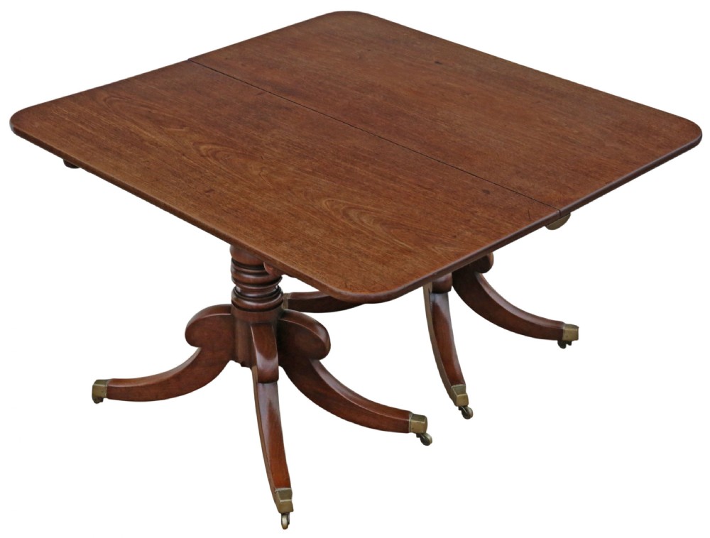 An early 19th-century Georgian mahogany twin pedestal dining table featuring turned columns, splayed legs, and brass cap castors. View X